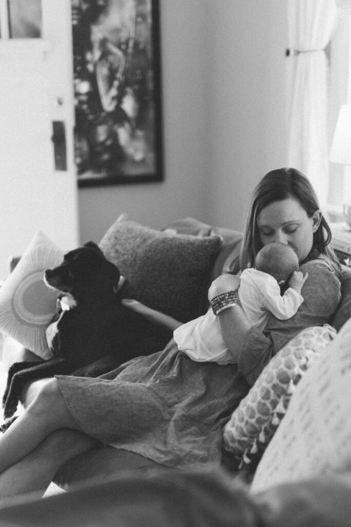 Newborn mom kisses baby while petting dog