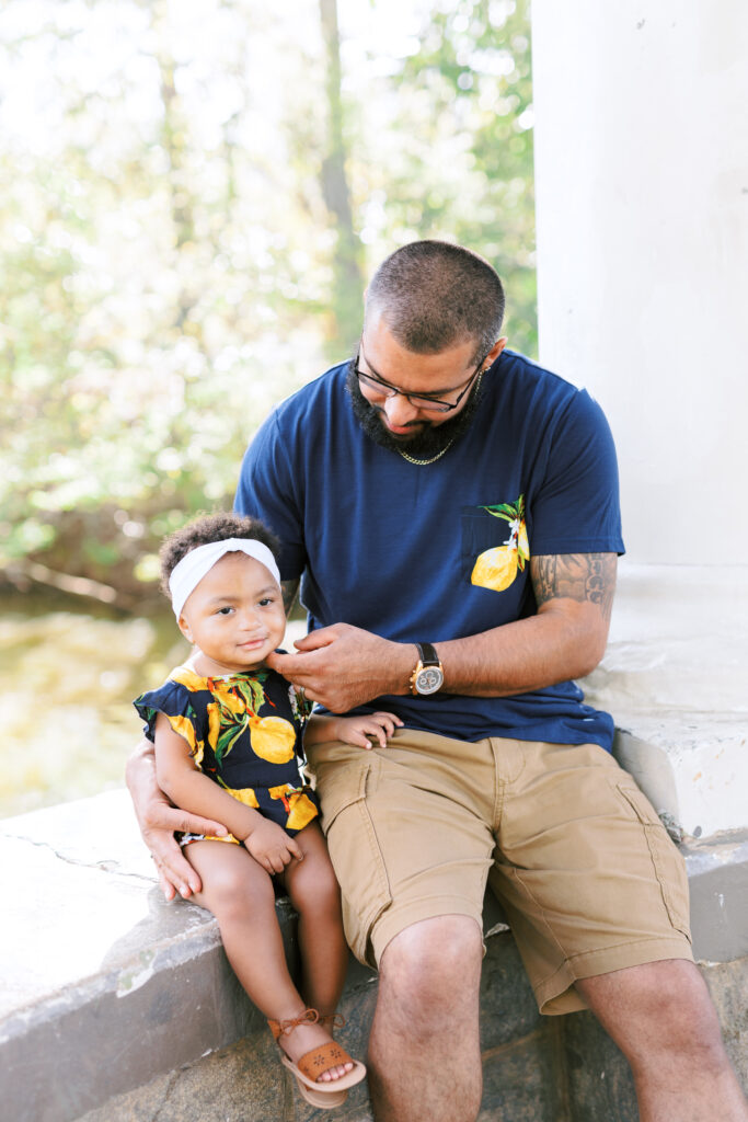 Dad brushes daughter's cheek in matching lemon outfits during family session at gazebo over Lake Clara Meer in Piedmont Park