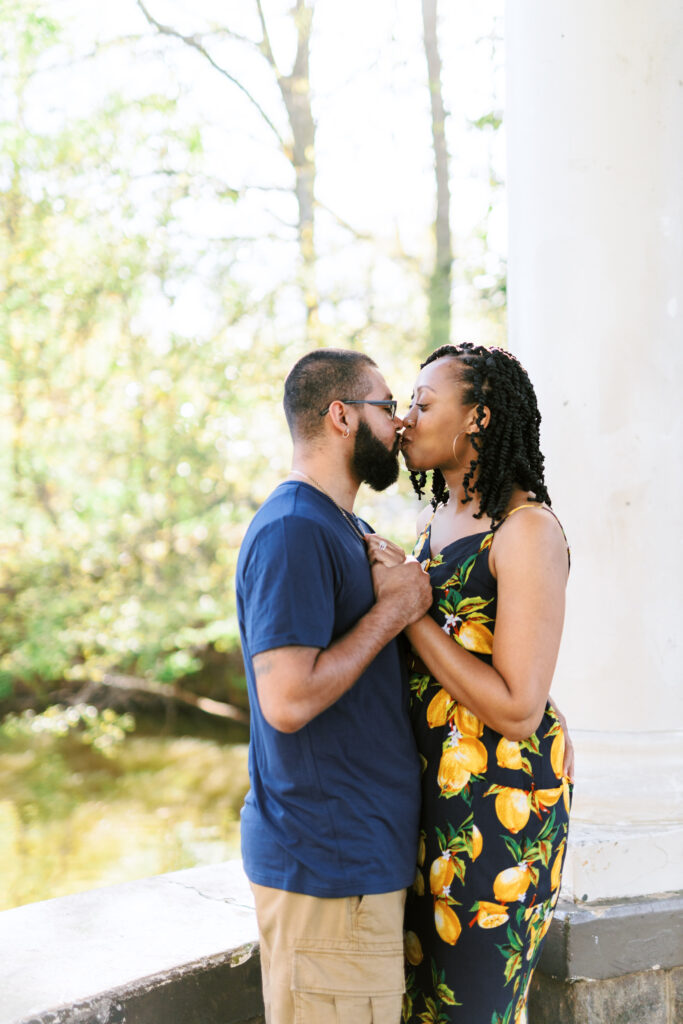 Mom and Dad kiss during family session at gazebo over Lake Clara Meer in Atlanta, Georgia