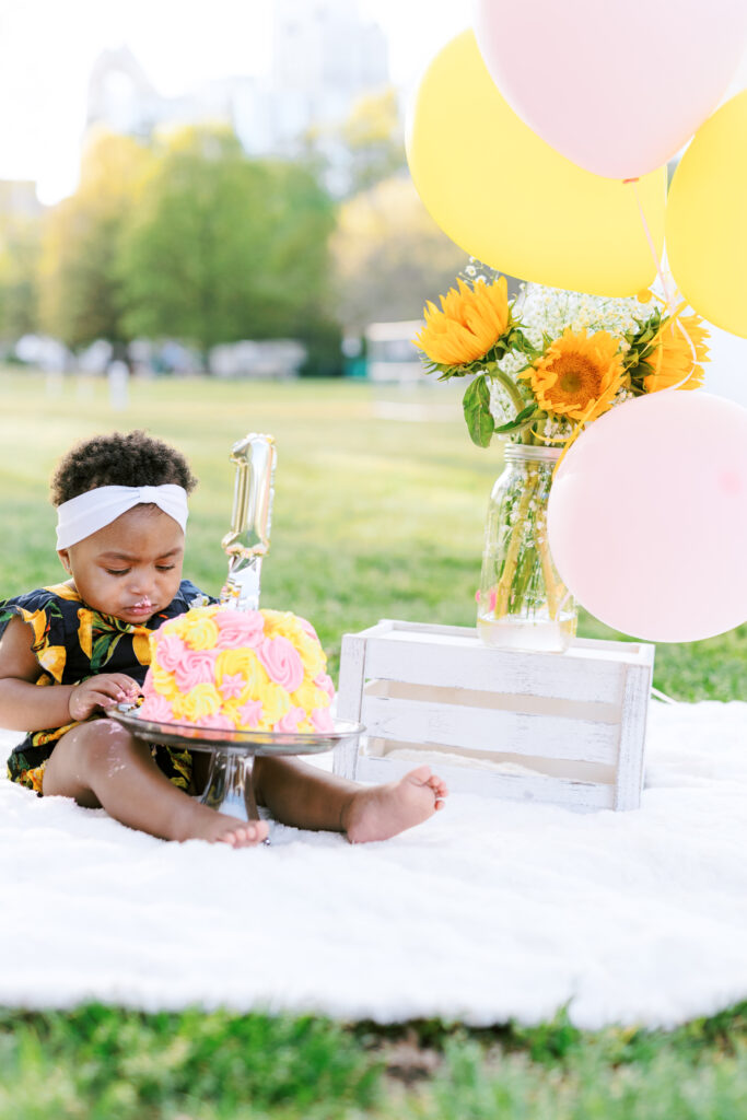 Baby girl looks at first birthday smash cake during milestones photo session in Atlanta, Georgia