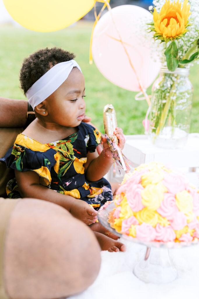 Baby girl smashes first birthday smash cake during milestones photo session at Piedmont Park in Atlanta, Georgia