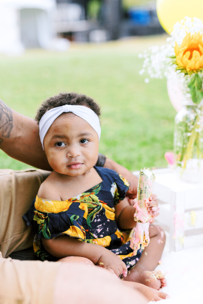 Baby girl smashes first birthday smash cake during milestones photo session at Piedmont Park in Atlanta, Georgia