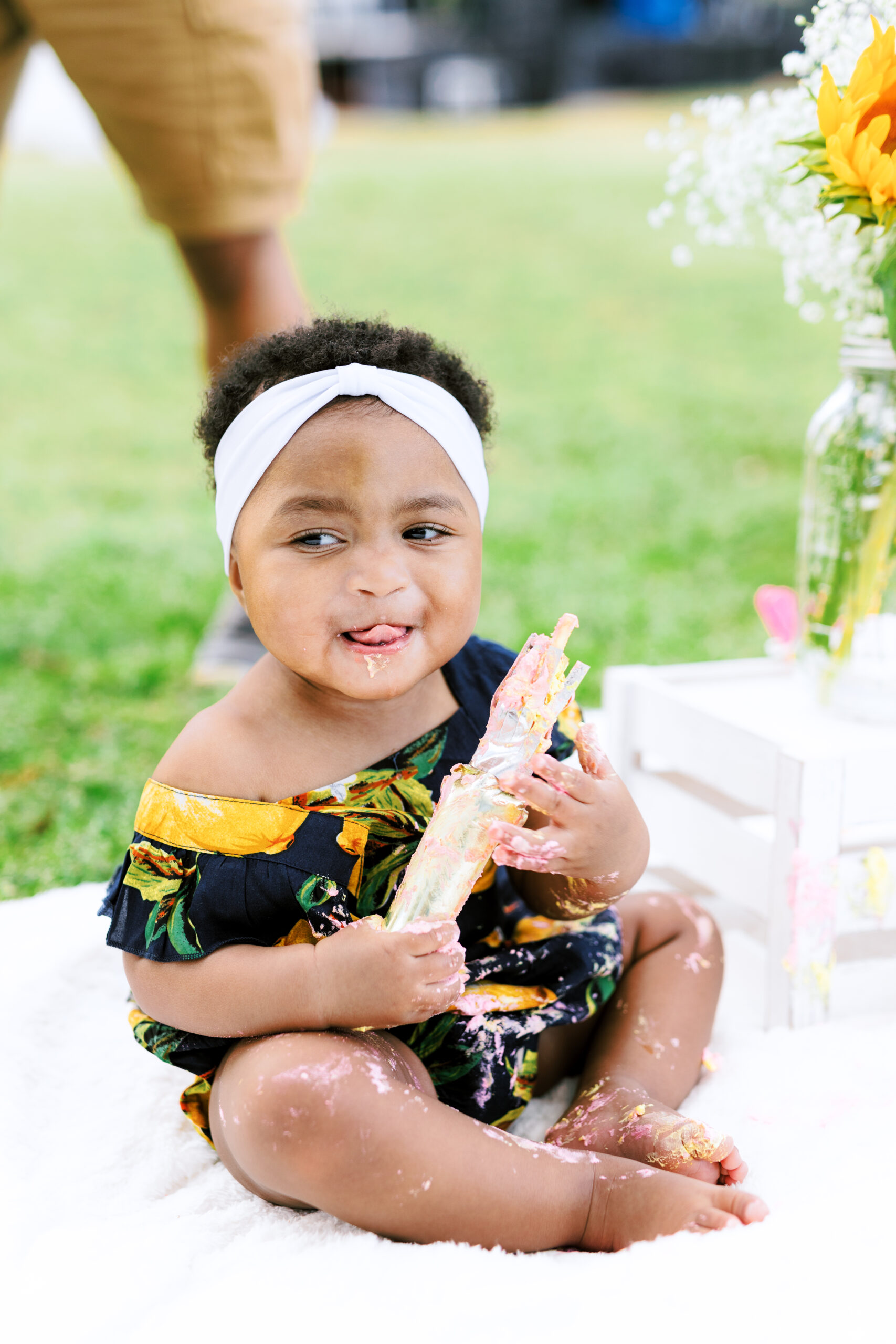 Baby girl licks icing of first birthday smash cake during milestones photo session at Piedmont Park in Atlanta, Georgia