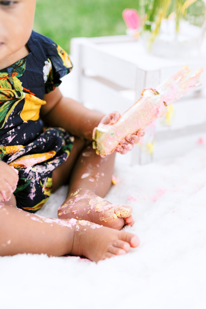 Baby girl licks icing of first birthday smash cake during milestones photo session at Piedmont Park in Atlanta, Georgia