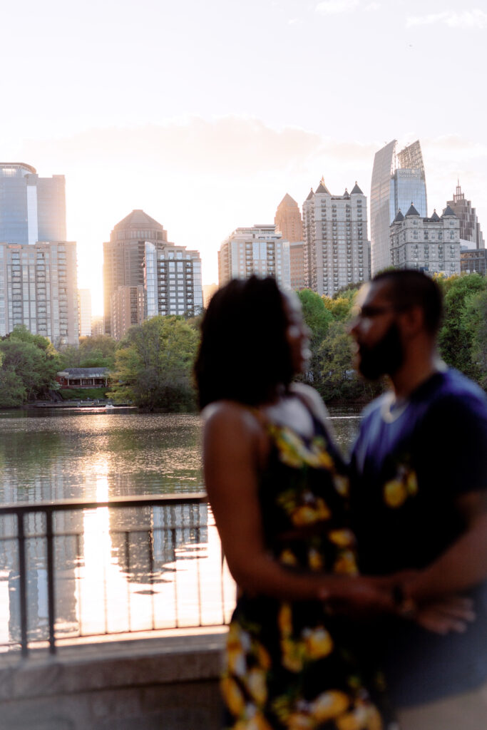 Couple smiles at each other at sunset in front of Atlanta Skyline at Piedmont Park