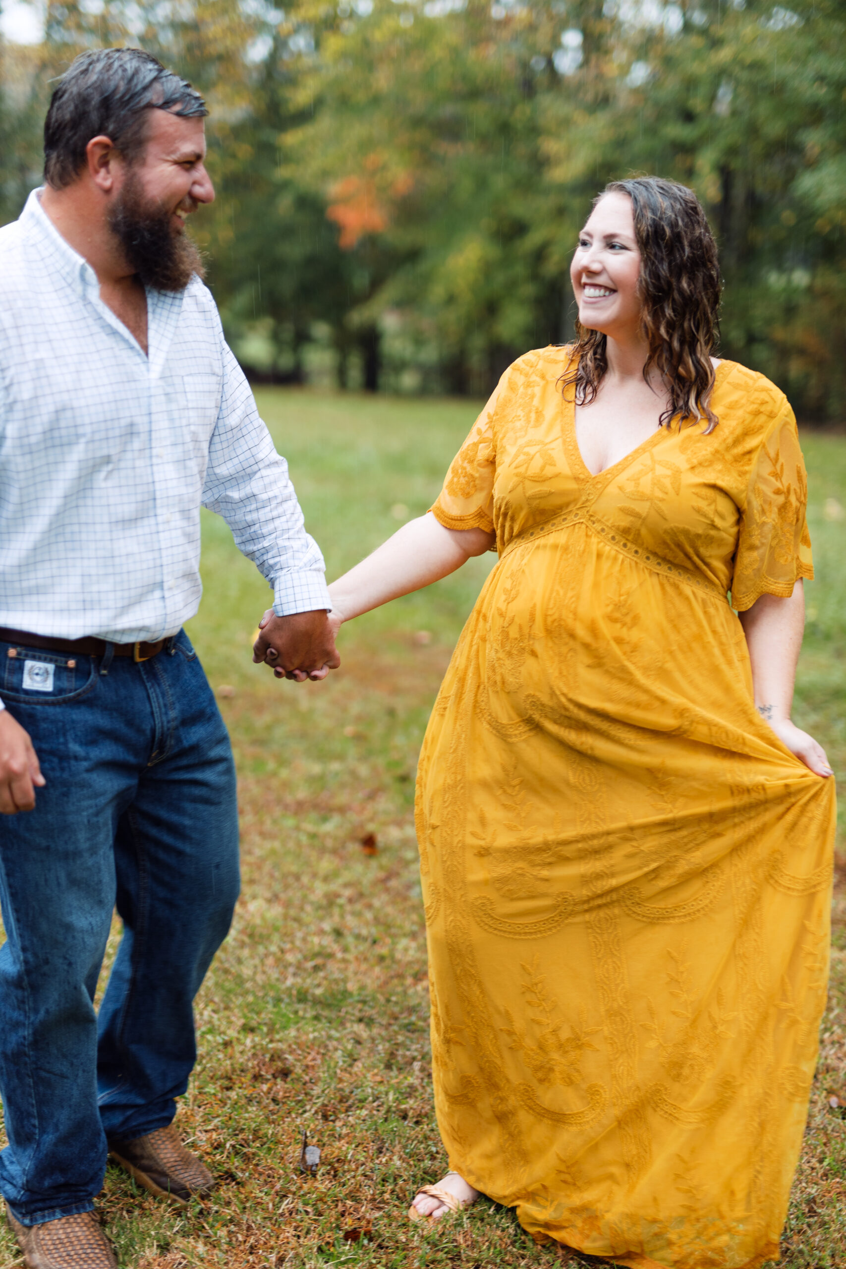 Maternity photoshoot in the rain with fall trees behind them