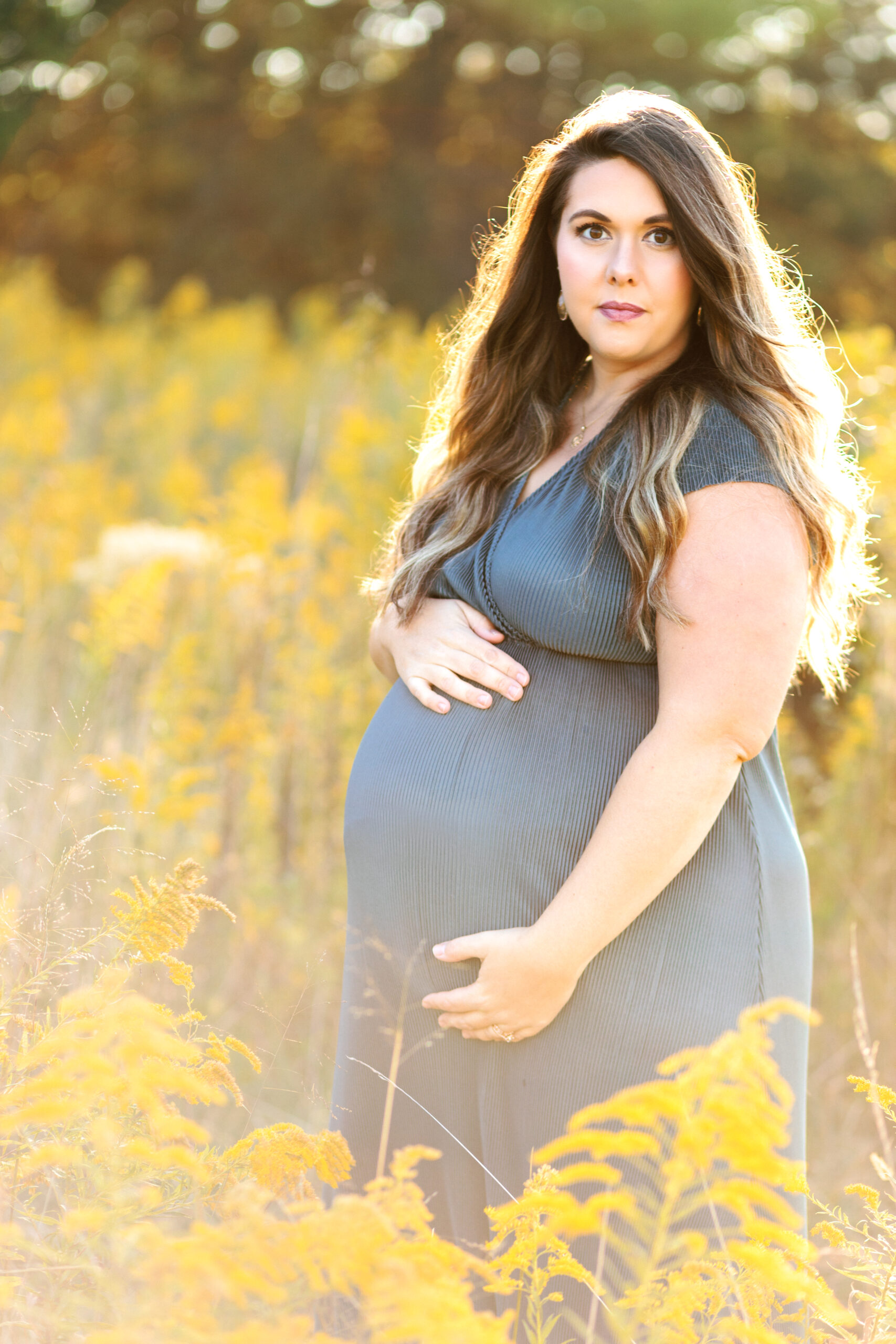 Beautiful pregnant mom holds belly in sunlight at Green Meadows Preserve