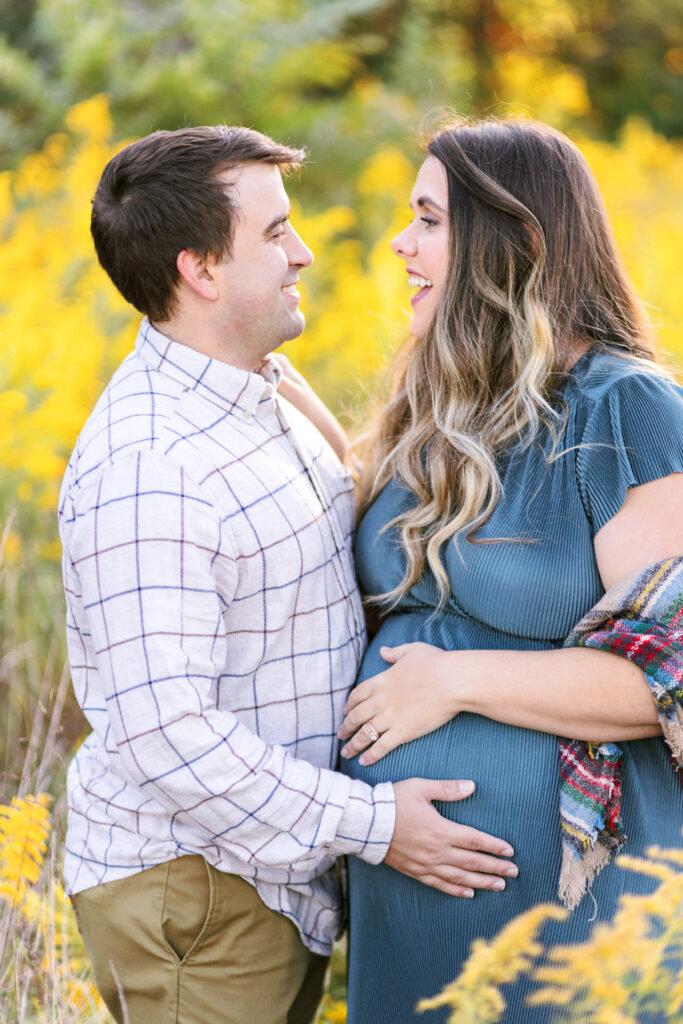 Expecting parents smile at each other during maternity photoshoot at Green Meadows Preserve