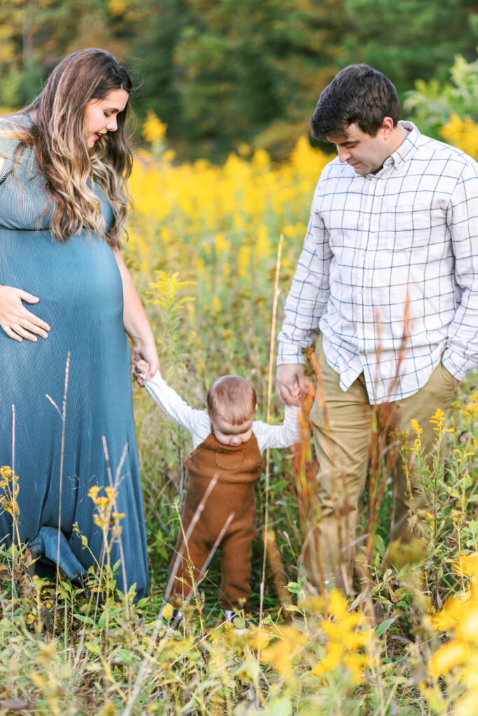 Family walks through yellow flower field during motherhood photoshoot at Green Meadows Preserve in Marietta, Georgia