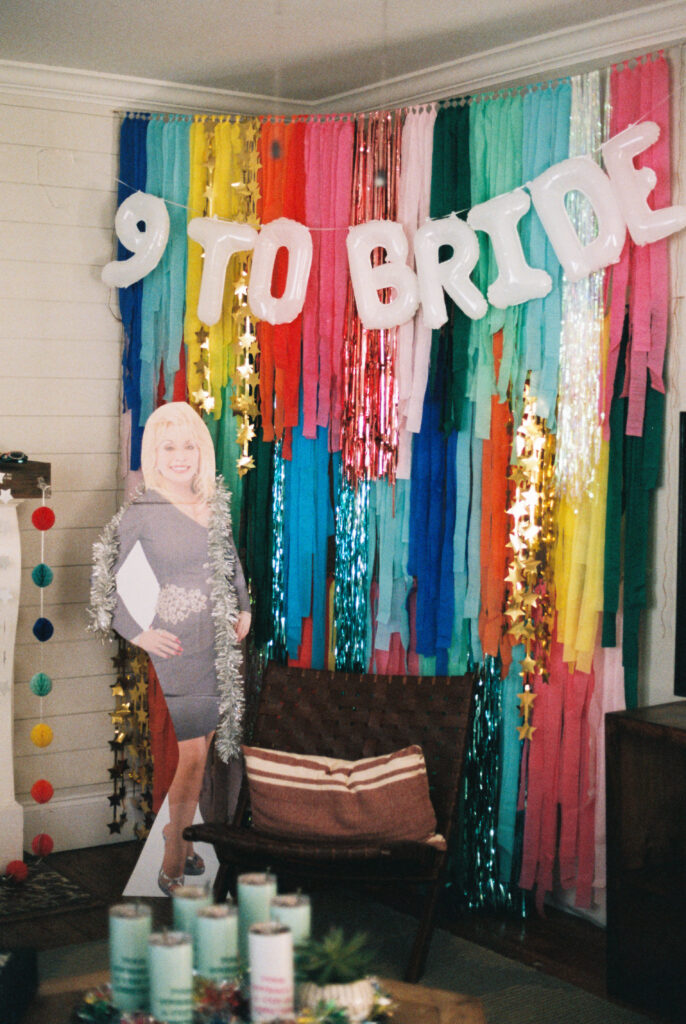 9-to-Bride; a Dolly Parton cardboard cutout stands in front of a Coat of Many Colors backdrop and 9-to-5 play on words for a Dolly Parton themed bachelorette party in Chattanooga, Tennessee