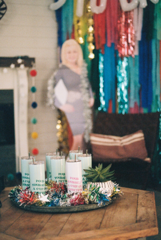 Custom drinking cups reading "cup of ambition" are displayed in front of a Dolly Parton cardboard cutout for a Dolly Parton themed bachelorette party in Chattanooga, Tennessee