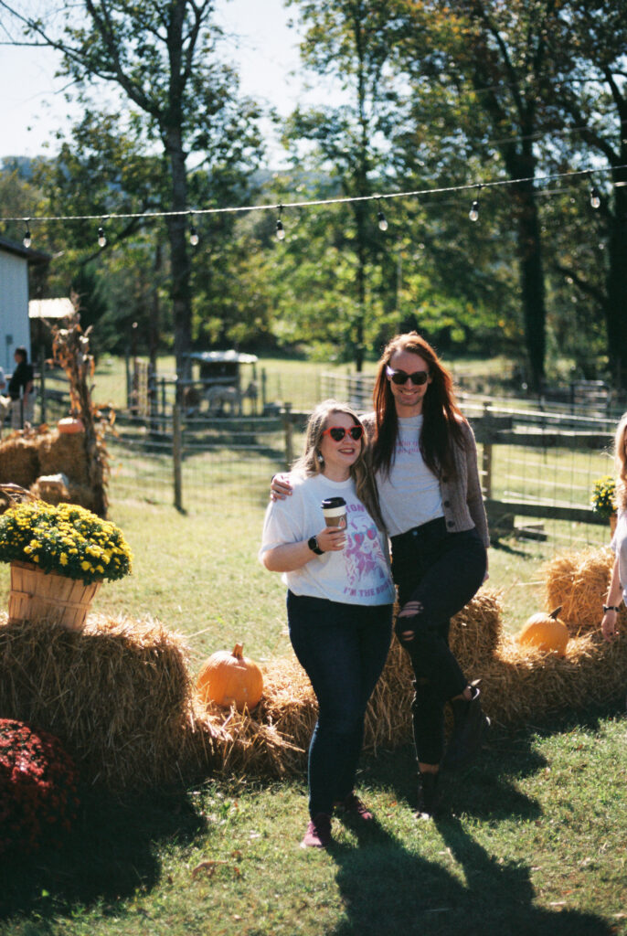 Friends laugh together at Alpaca farm on a Dolly Parton themed bachelorette party in Chattanooga, Tennessee in front of pumpkins and mums in October