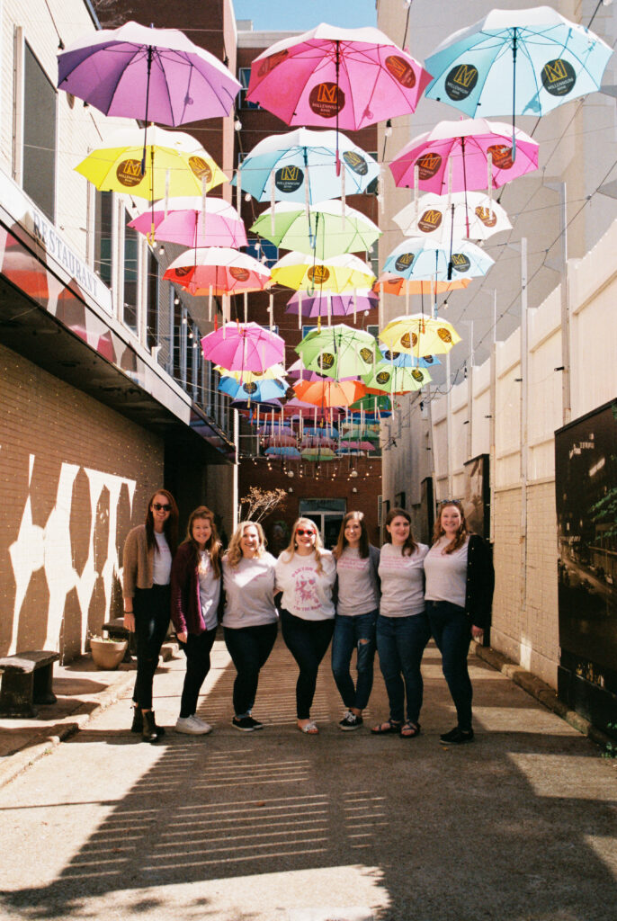 Group of bridesmaids smile together at Umbrella Alley on a Dolly Parton themed bachelorette party in Chattanooga, Tennessee