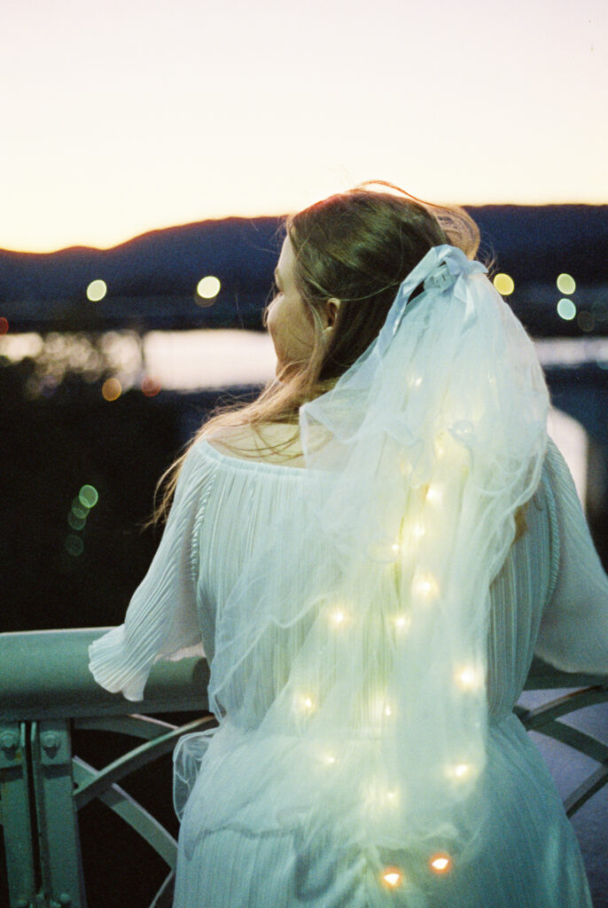 Bride looks out onto river in Chattanooga, Tennessee with light-up veil on a Dolly Parton themed bachelorette party in Chattanooga, Tennessee